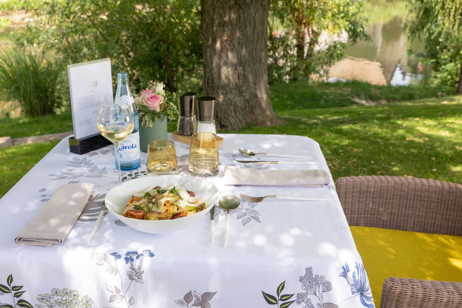 Petit-déjeuner matinal servi sur une table avec une nappe fleurie, sur la terrasse au bord de l'Ill à l'Hôtel des Berges en Alsace